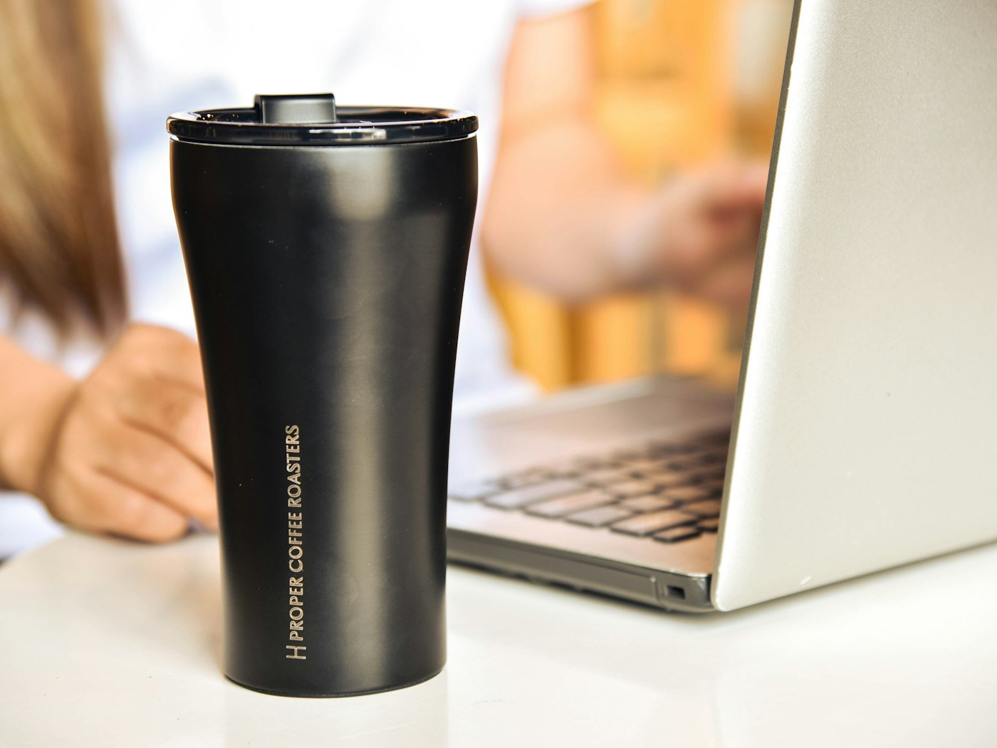 Black branded tumbler on a work desk beside a laptop